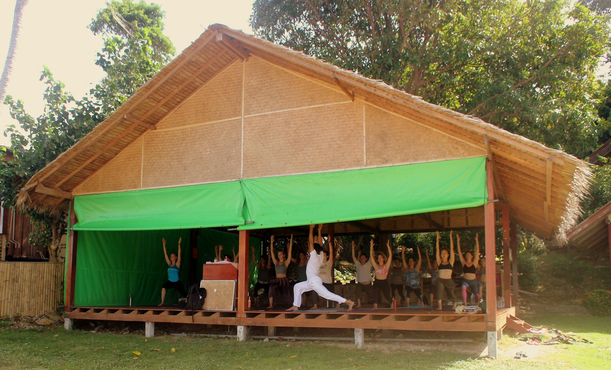 Group yoga session in a bamboo pavilion in Thailand, demonstrating warrior pose for well-being.