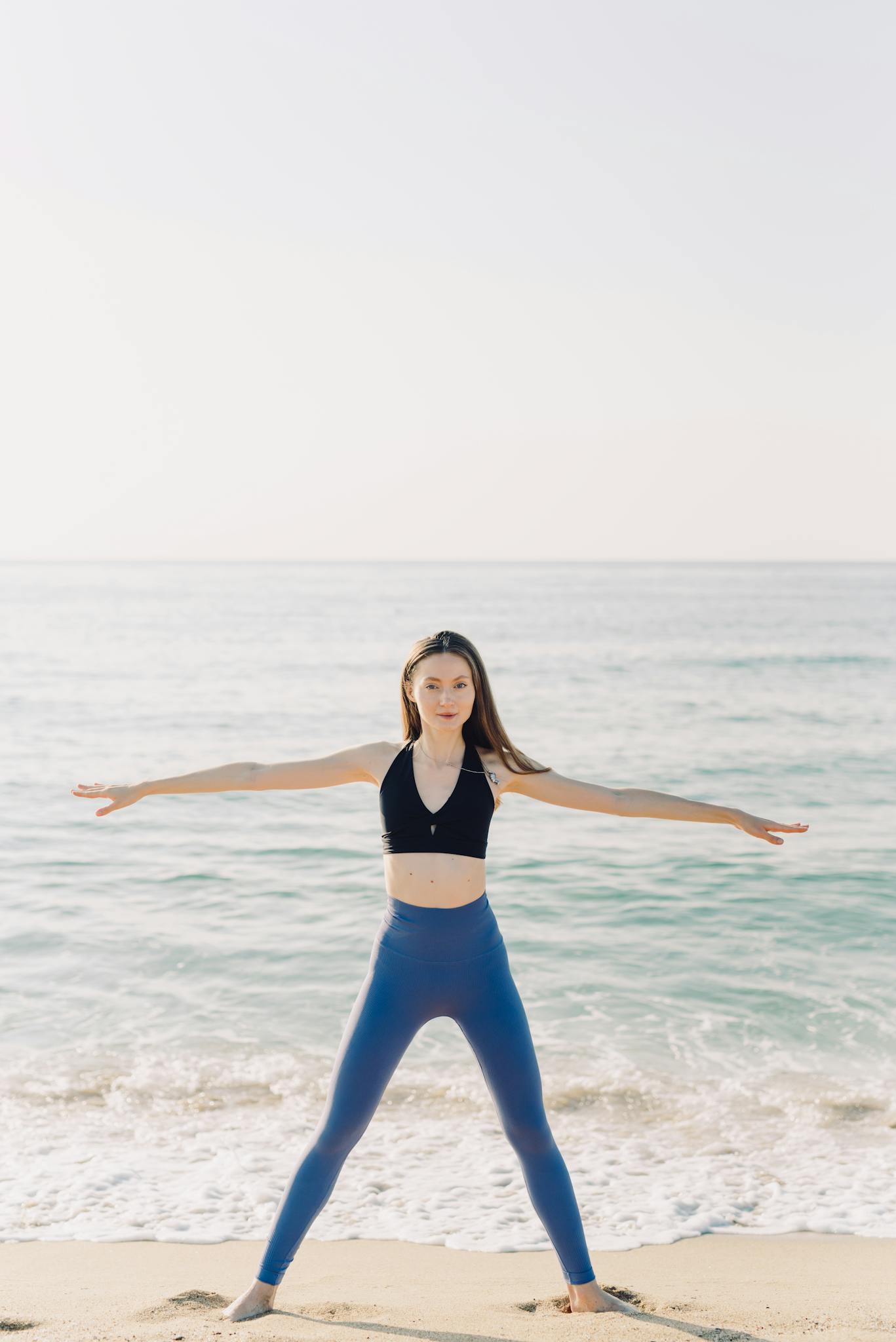 Woman in yoga pose enjoying ocean view on a sunny beach, promoting wellness and healthy lifestyle.